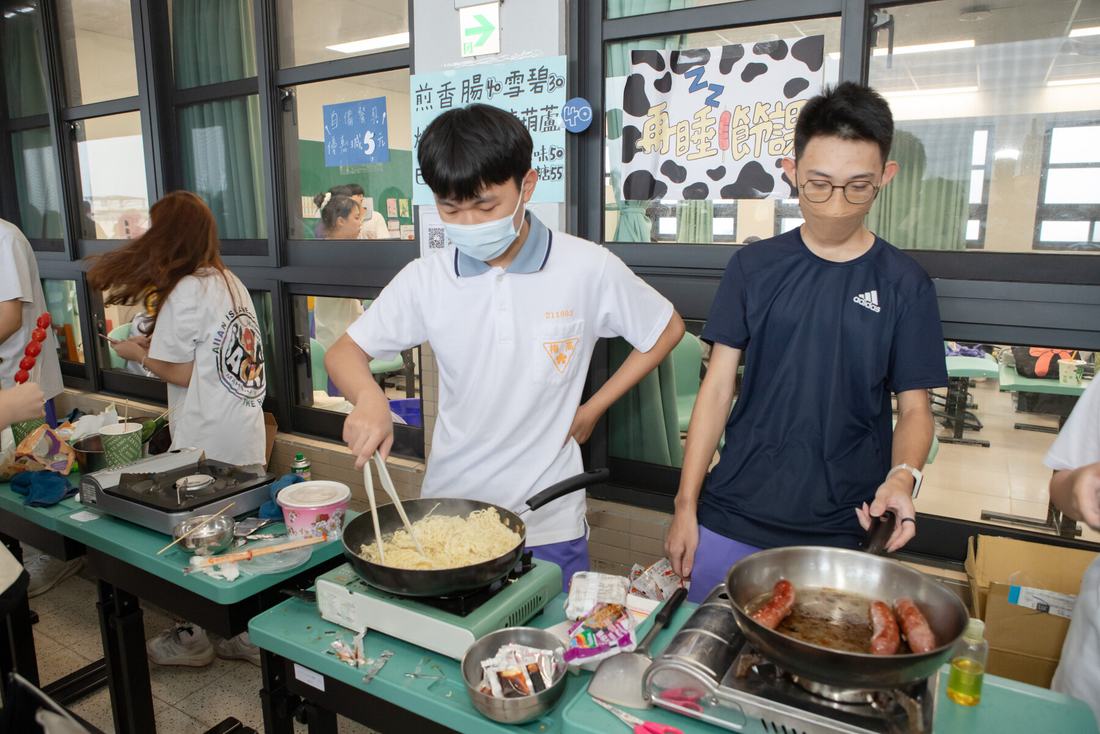 兩名學生在攤位的大鍋前翻炒料理。
