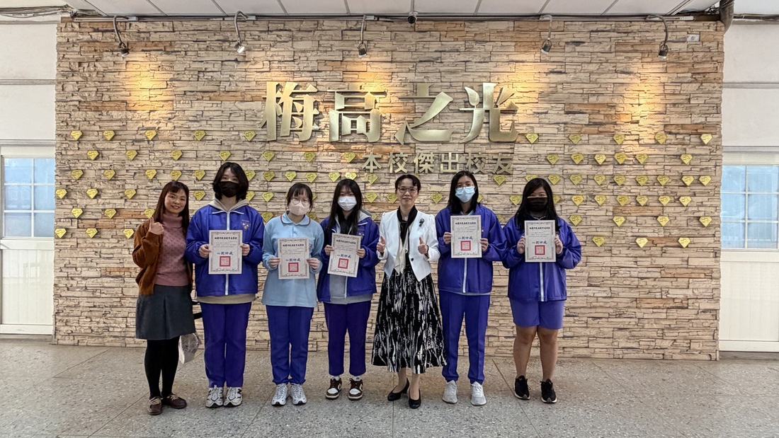 在刻有「梅高之光」字樣的石牆前，學生手持獎狀與師長合影。
