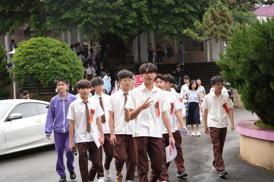 畢業生在校園中庭邊走邊聊，手持畢業紀念品。