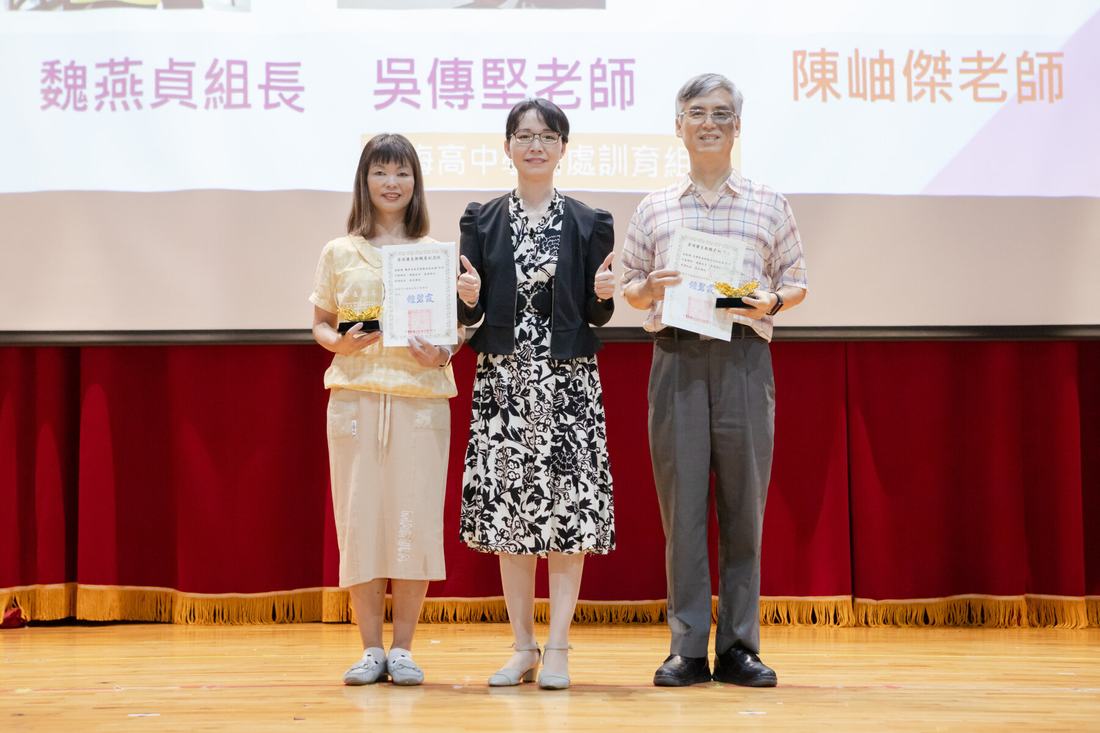 禮堂舞台上，師長手持獎狀合影，投影幕顯示受獎名單。