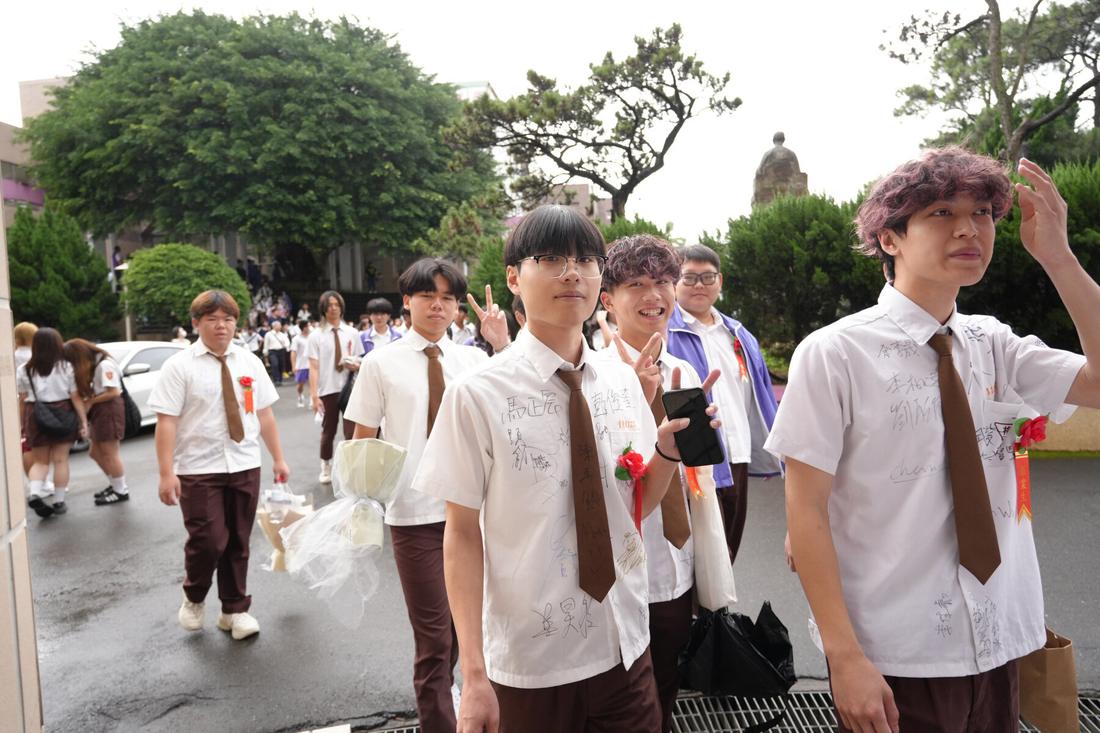 雨天的校園步道上，穿著制服配戴胸花的畢業生結伴而行。