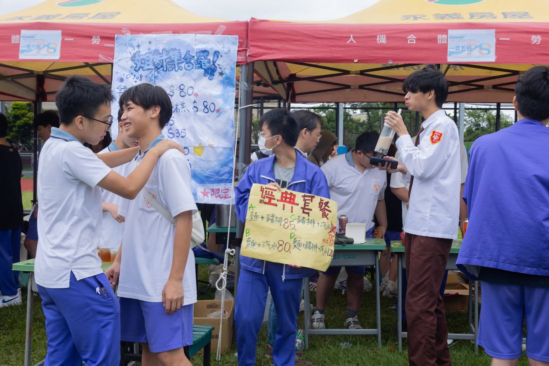 攤位前學生進行互動遊戲，旁有手繪指示牌。