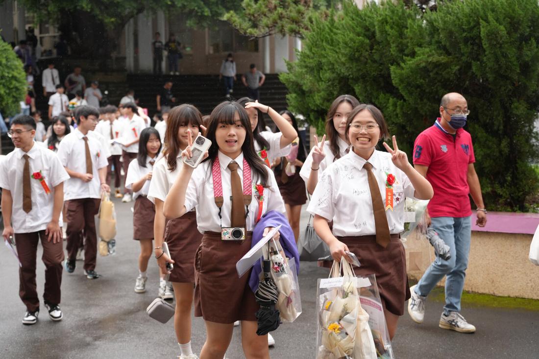 畢業生撐傘走過校園廣場，手上提著紀念品。