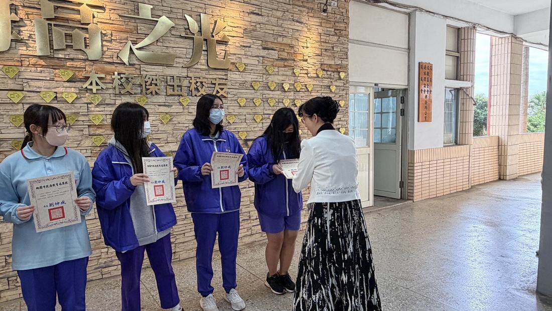 教師在梅高之光牆前將獎狀交給學生。