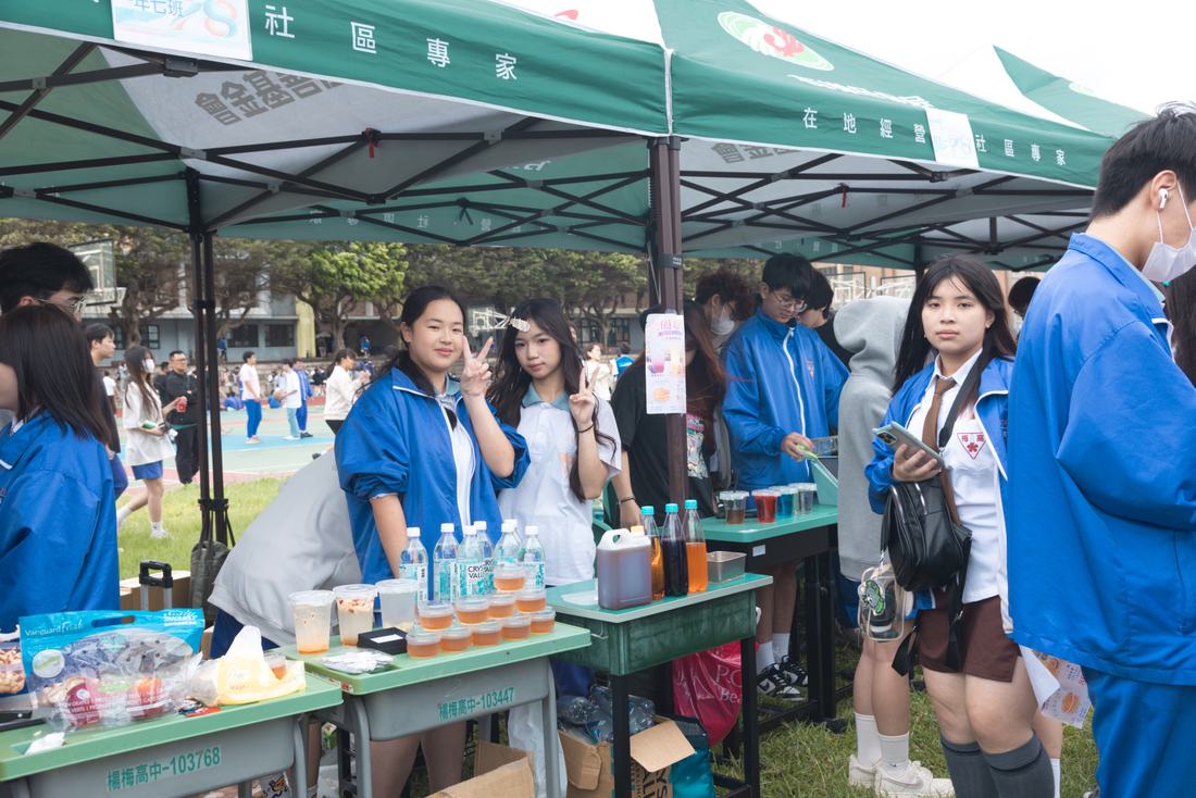 綠色帳篷下的社團攤位，學生在桌前服務來賓。