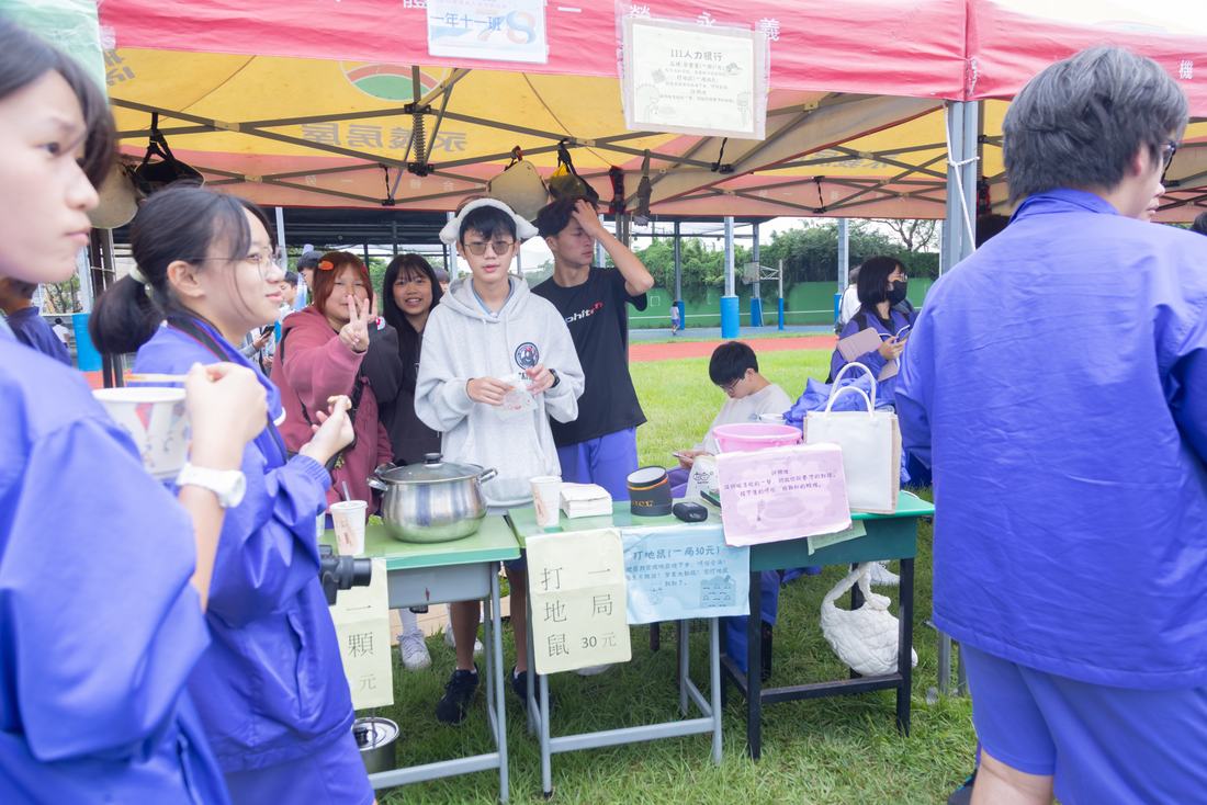 戶外帳篷攤位前，學生正在整理桌面與商品。