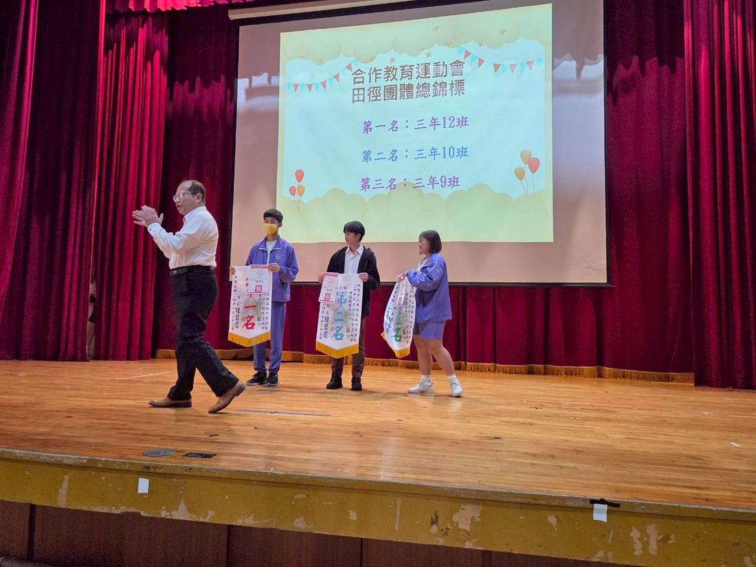 教師持麥克風在舞台上宣讀得獎名單，學生在旁等候。