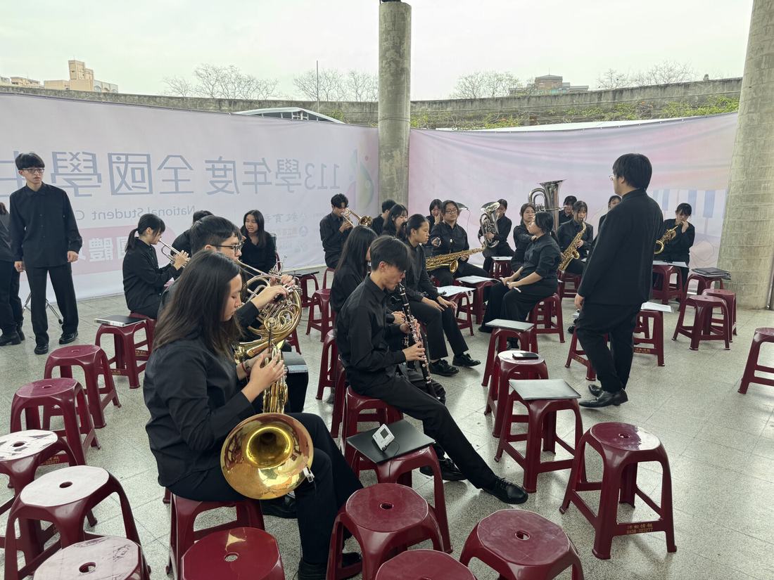 戶外準備區，團員坐在紅色圓凳上調音與整備樂器。