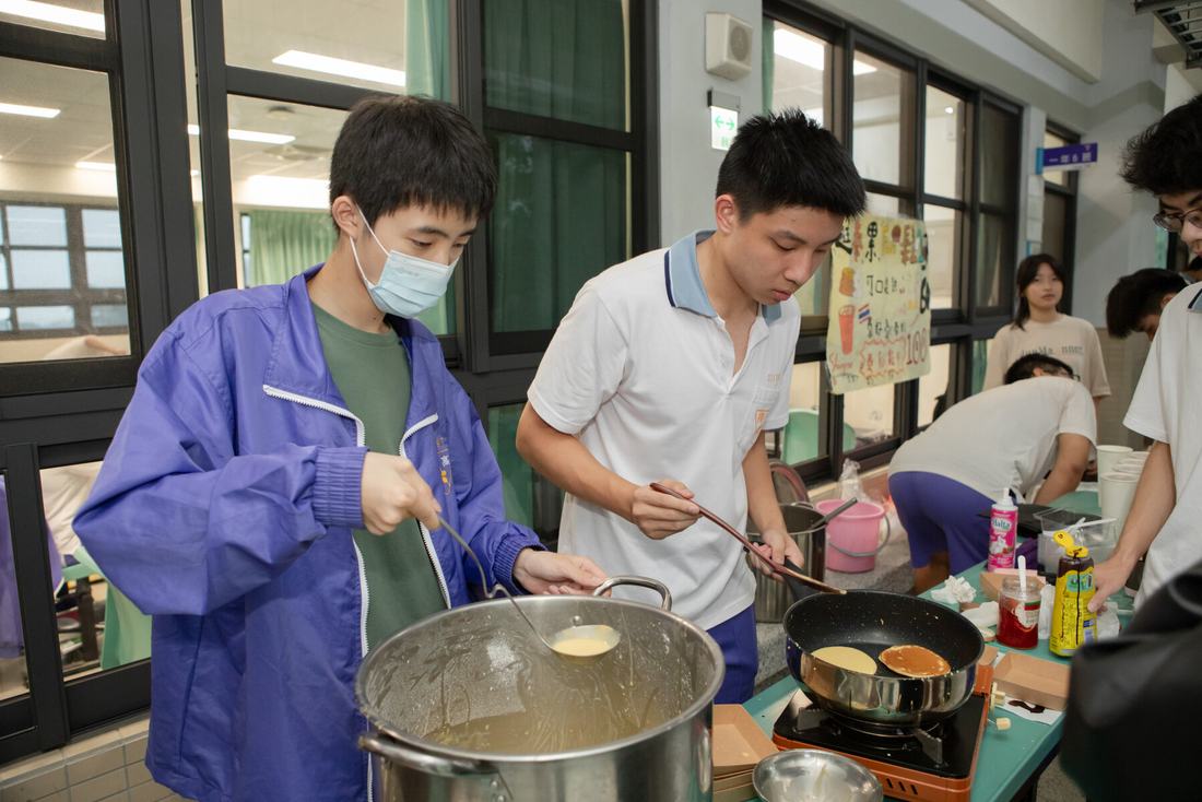 兩名學生在攤位大鍋前料理食物。