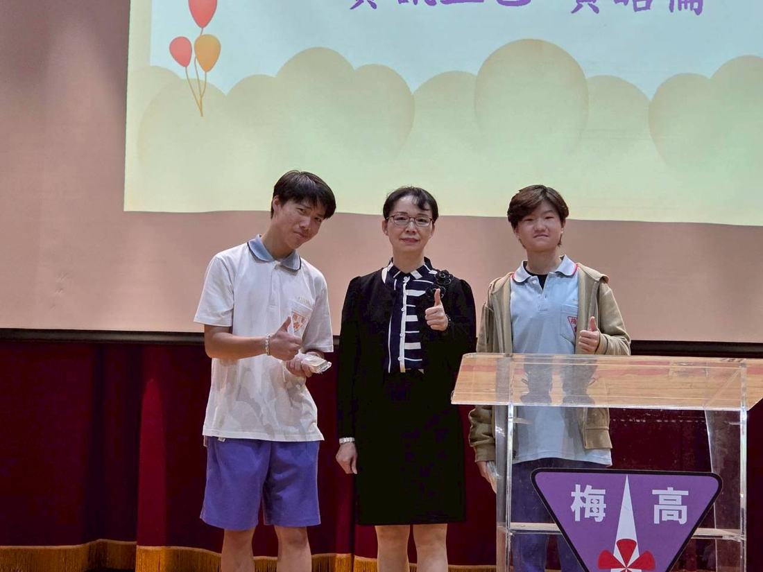 舞台講台旁，教師與兩名學生一同合影。