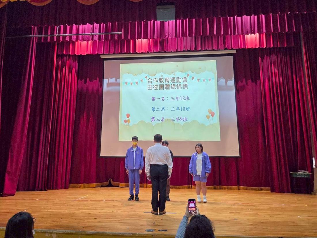 兩名學生走上舞台接受頒獎，投影幕顯示活動資訊。